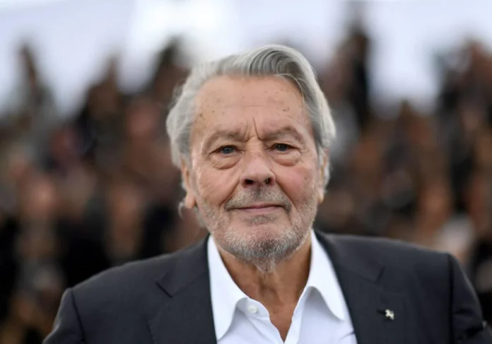 Alain Delon, icónico actor francés, en primer plano con traje oscuro y camisa blanca, mostrando su rostro envejecido pero distinguido.