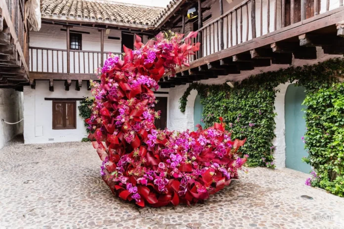 Escultura floral en forma de media luna hecha con flores de color rosa y rojo en un patio andaluz decorado para el Festival Flora en Córdoba.