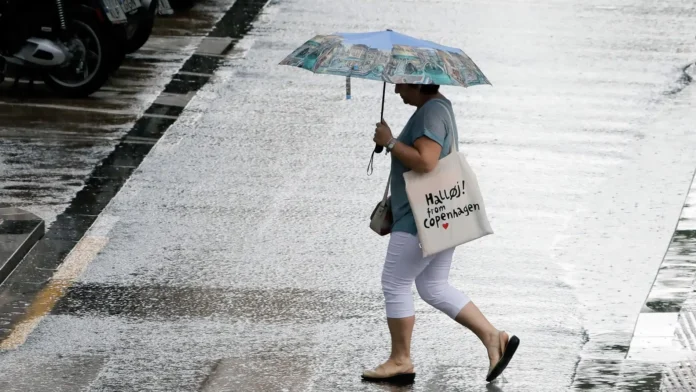 Turista con paraguas y bolsa de Copenhagen caminando bajo la lluvia en calle inundada