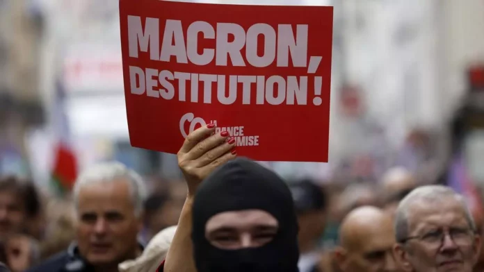 Manifestante sosteniendo pancarta roja exigiendo la destitución de Macron en protesta masiva en Francia