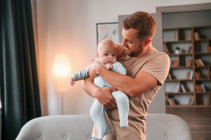 Padre joven cuidando a su bebé en casa, simbolizando el aumento en el uso del permiso parental por parte de los hombres en España.