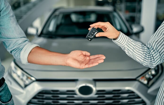 Vendedor entregando llaves de coche nuevo a comprador en concesionario