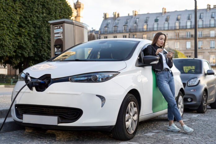 Mujer junto a un coche eléctrico cargando en una estación de carga urbana