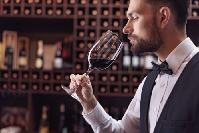 Experto en vinos evaluando un vino tinto en copa de cristal frente a una bodega
