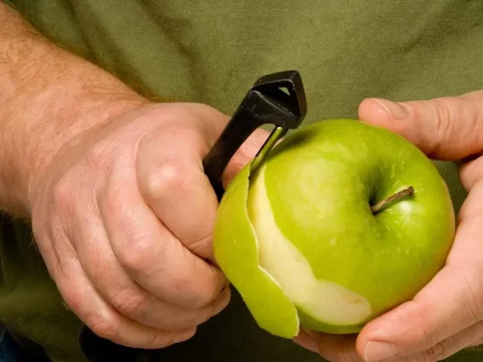 Manos sosteniendo una manzana parcialmente pelada, mostrando el contraste entre la piel y la pulpa